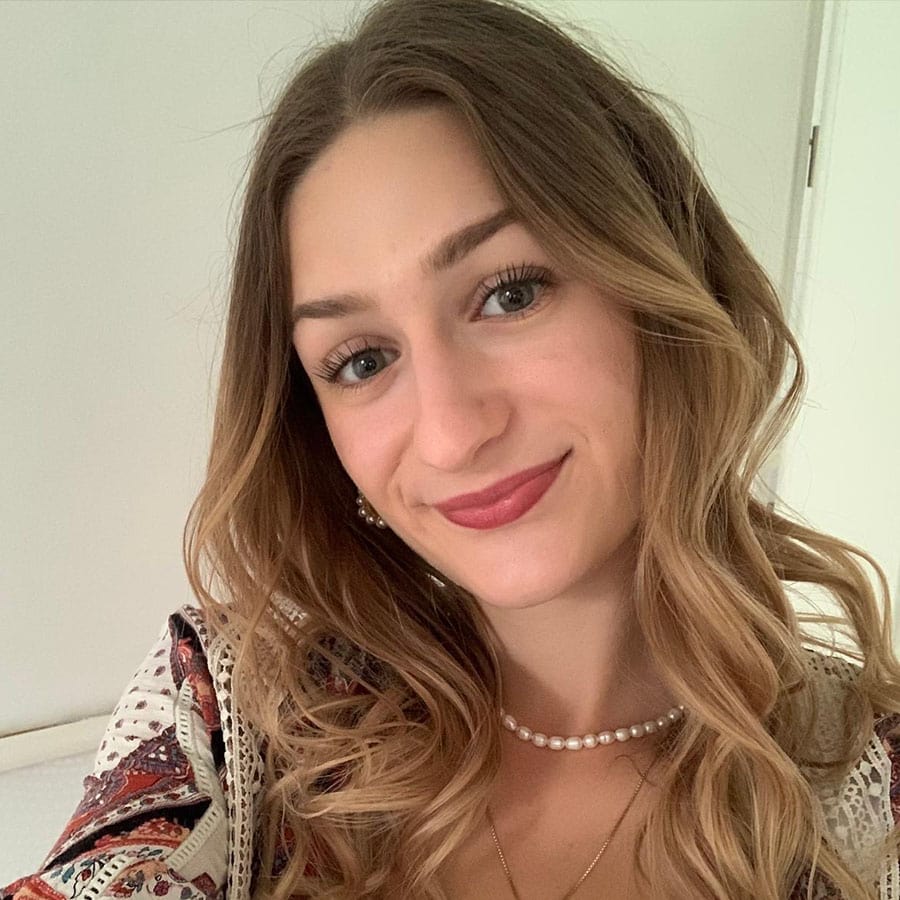 Schöne junge Frau mit lockigem Haar und Perlenkette, lächelnd, im Innenraum.