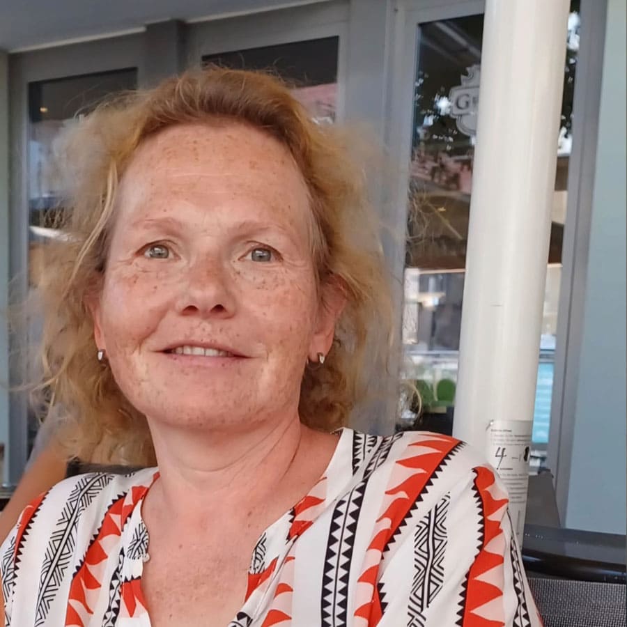 Ein freundliches Porträt einer Frau mit roten Haaren vor einem Kosmetikstudio in Duisburg.